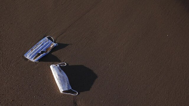 Blue and white used dispoable medical face masks thrown away laying on wet sand of sea beach outdoor