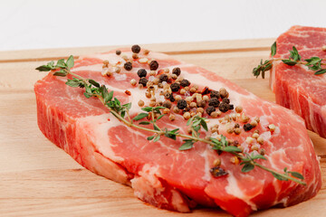 fresh chopped raw pork steaks with spices and thyme on a cutting kitchen board on a white wooden table