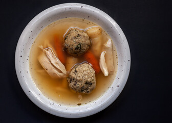 Traditional Czech and Slovak homemade chicken soup with vegetables and liver dumplings in a white plate on the black background.