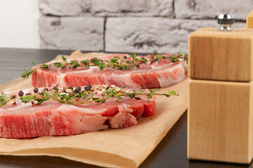 fresh raw marbled meat pork steak with thyme and seasoning on brown parchment paper on a black table against a gray brick wall background