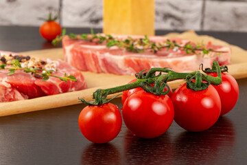 freshly chopped raw pork steaks with spices and thyme on a sheet of parchment. next to ripe red tomatoes and a salt shaker