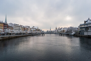 Waterside view of snow covered Zurich city Switzerland from a bridge crossing the Limmat river winter time cloudy day