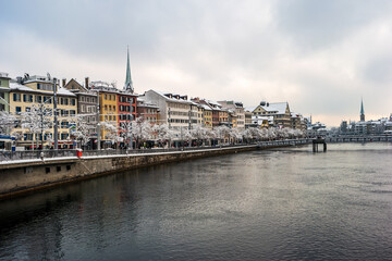Fototapeta na wymiar Waterside view of snow covered Zurich city Switzerland from a bridge crossing the Limmat river winter time cloudy day