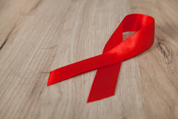 Red ribbon - symbol of awareness and support for those living with HIV, wooden background.