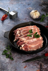 Raw pork meat slices with spices and herbs in a black pan. Black background. Top view space for text