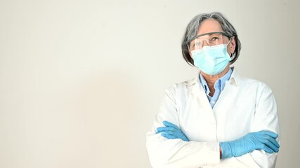 Confident senior female doctor in white professional coat, wearing protective mask, goggles and gloves crossed her arms and looking at the camera, isolated. Fight against coronavirus and viral disease