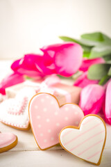 Fototapeta premium Valentine Day concept, Spring Woman Day Holiday, Mothers Day background, Red tulip flowers bouquet, craft paper gift box, heart shaped traditional sugar cookies, White wooden background copy space
