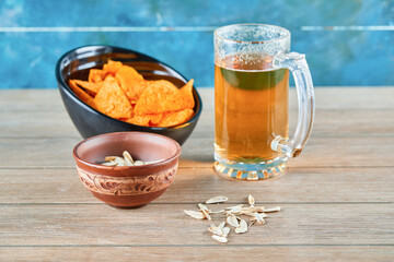 Sunflower seeds, a bowl of chips and a glass of beer on wooden table