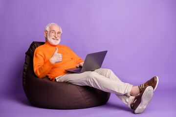 Full body profile portrait of positive man sit soft chair show thumb up wear pants shoes isolated on purple color background