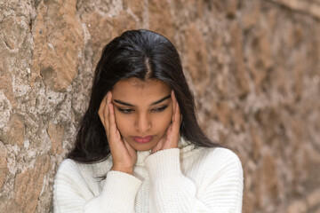Close up portrait of a brunette woman rubbing her temples to alleviate an awful headache. Outdoors