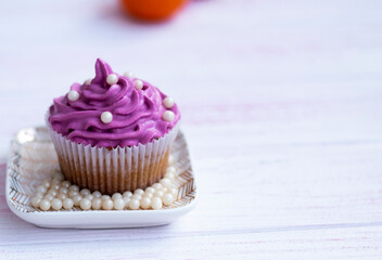 muffin with lilac color cream decorated with edible pearls on a saucer stands on a wooden background. Festive cake with cream. cream cheese, butter cream. Fresh bakery. Birthday dessert. small cake. 