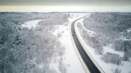 View from the drone on the paved road, cars, winter snow-covered forest, village. Beautiful winter landscape with paved road
