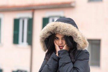 Cute young woman freezing in winter coat standing in street