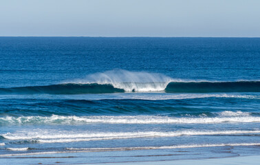 Wave breaking on a bright sunny morning. Perfect wave barrel with offshore wind on a sand beach break