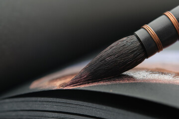 Close up of a artistic paintbrush for watercolor painting. Painting with a brush in a sketchbook on black paper sheet. - 408313638