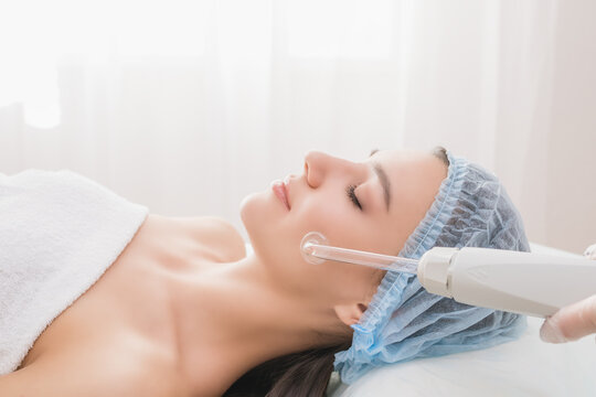 Beautiful young woman receiving darsonval procedure electric massage at beauty salon. Hardware cosmetology. Selective focus.