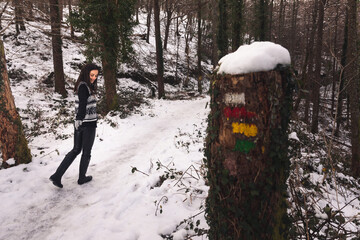 Young girl walking on a snowy forest following a path marks.