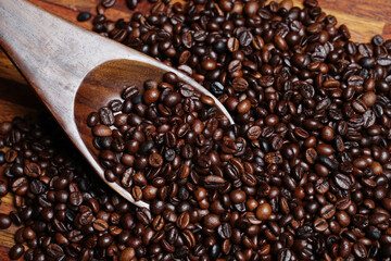Obraz premium Scoop out ripe coffee beans using a large spoon made of wood and iron. Coffee beans scattered on the floor. Details texture of dark brown coffee beans. Graphic resourches for design template.