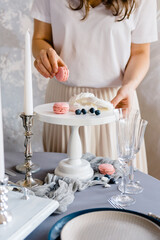 Female hands put macaroon on a wooden white cake stand. Exquisite serving.