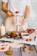 Obraz na płótnie Canvas Female hands hold strawberries on a wooden stand. A romantic candlelit breakfast on a tray with berries, tea and cookies.