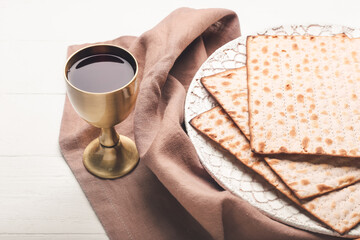 Plate with Jewish flatbread matza for Passover and cup of wine on white wooden background