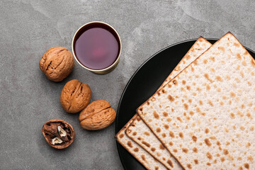 Plate with Jewish flatbread matza for Passover, cup of wine and walnuts on grey background