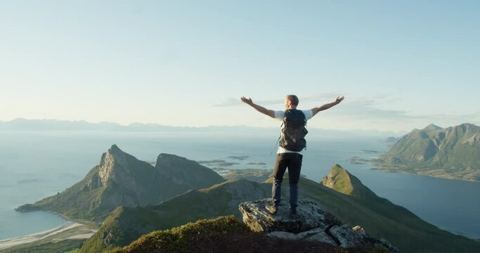 Norwegian man raising arms celebrating view of arctic mountains - static rear view