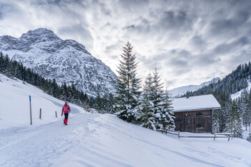 active senior woman hiking in the snowy mountains of Kleinwalsertal, Vorarlberg, Austria, near village of Baad, below the summit of Widderstein  
