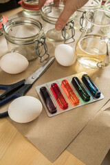 Frau mit Essig, Wasser und bunten Ostereier Kaltfarben in Rot, Orange, Gelb, Blau, Grün in Verpackung auf Papier Unterlage mit Gläser, gekochte Eier und Schere zum Färben zu Ostern