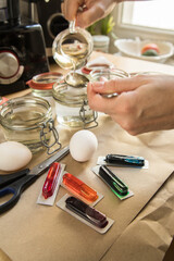 Frau mit L&ouml;ffel, Essig, Wasser und bunten Ostereier Kaltfarben in Rot, Orange, Gelb, Blau, Gr&uuml;n in Verpackung auf Papier Unterlage mit gekochte Eier und Schere zum F&auml;rben zu Ostern