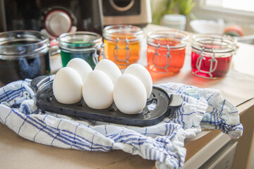 Gekochte Eier und bunte Ostereier Kaltfarben in Rot, Orange, Gelb, Blau, Grün in Glas auf Papier Unterlage in Küche zum Färben zu Ostern
