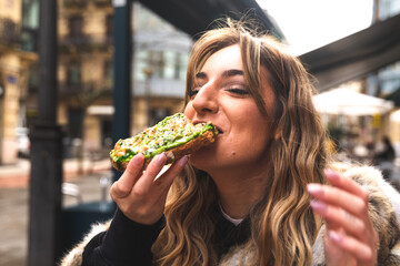 Young caucasian woman having breakfast at a terrace eating an avocado toast.
