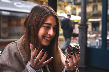 Young caucasian girl enjoying a chocolate cupcake having breakfast at a terrace outdoors.