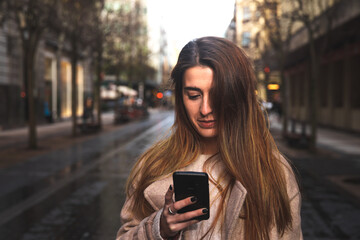 Obraz premium Young caucasian brunette woman using a smartphone at the street