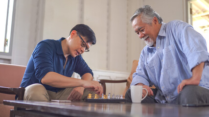 Asian Senior man playing chess with son