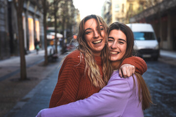 Two friends smiling and embracing each other at the street