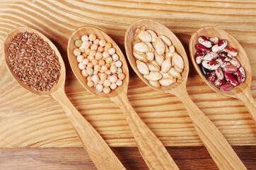 Four wooden spoons with various seeds of wheat, peas, pumpkin, beans.