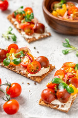 Crispbreads with feta cheese, colorful cherry tomatoes, onions, and herbs close-up. Toast with cream cheese and tomatoes on a gray background. Tasty breakfast or snack.