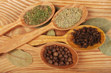 Four wooden spoons with various spices on a wooden table.