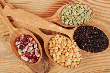 Four wooden spoons with a variety of legumes and grains. Beans, corn, peas.