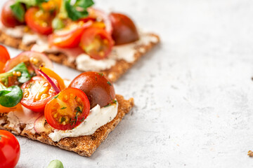 Crispbreads with feta cheese, colorful cherry tomatoes, onions, and herbs close-up. Toast with cream cheese and tomatoes on a gray background. Copy space for text. Tasty breakfast or snack.