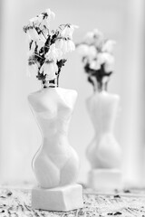 a white vase in the shape of a woman silhouette stands on a table, it has a set of white withered flowers
