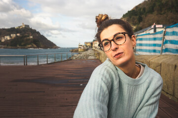 Fototapeta premium Portrait of a young caucasian girl sat on a bench at the sea side on Donostia-San Sebastian; Basque Country.