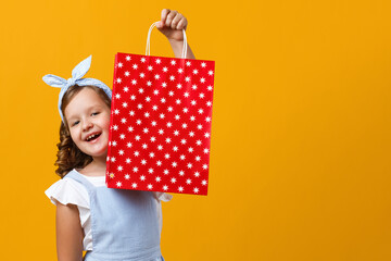 Fototapeta premium Cheerful girl in holding a paper bag with the purchase. Cute child on a yellow background.