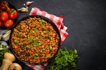 Bolognese sauce in iron plate at black table top view. Traditional italian meal, main ingredient for pasta bolognese.