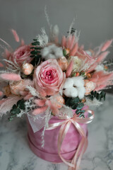 A bouquet of flowers of pink shades of roses and dried flowers in a gift box.