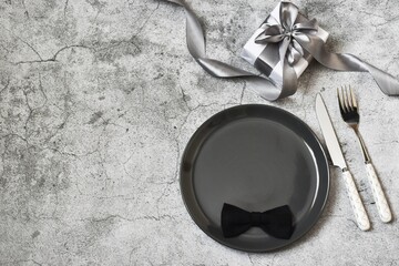 Fathers day concept. Table setting - plate, gift box, cutlery on grey concrete background. Top view, flat lay, copy space. 