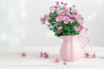 Pink chrysanthemum flowers in a pink pitcher on a white wooden table with a copy space