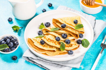 Crepes with blueberries and honey at blue table. Healthy breakfast or snack.