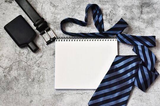 Happy Father's Day. Notepad with tie and belt, cologne on gray concrete background. Greetings and gifts